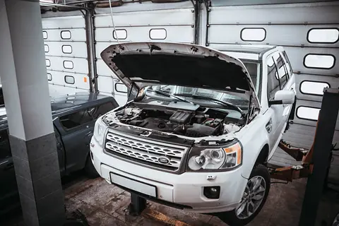 Автомобиль с открытым капотом на подъёмнике в боксе сервиса, за ним секционные ворота