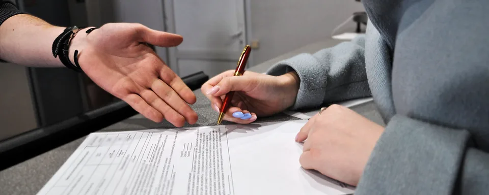 Клиентка подписывает бланк на стойке приёмки, сотрудник сервиса показывает строку для подписи