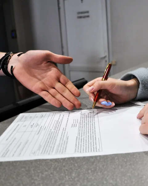 Клиентка подписывает бланк на стойке приёмки, сотрудник показывает строку для подписи