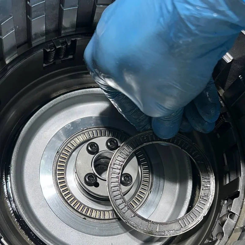 Рука мастера в перчатке вынимает подшипник из барабана коробки-автомата